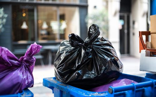Purple and black bags of trash on a garbage bin during daytime